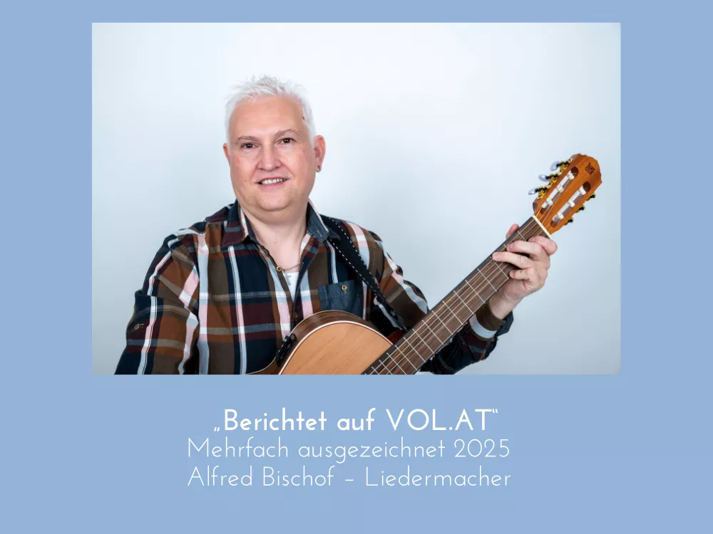 Alfred Bischof, Vorarlberger Liedermacher, lächelnd mit Konzertgitarre, braunkariertes Hemd, Pressefoto im Zusammenhang mit Bericht auf VOL.AT