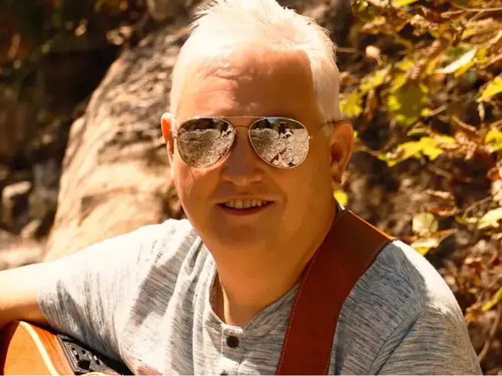 Liedermacher Alfred Bischof mit Gitarre draußen – Natur, Musik und ehrliche Worte